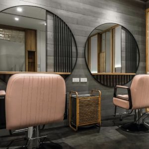 Modern salon interior with pink styling chairs, round mirrors, and dark wood panel walls.