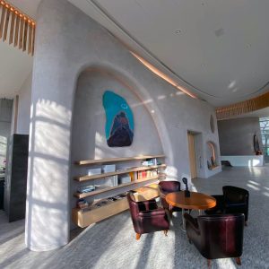 Modern living space with curved walls, large windows, a bookshelf, and a round table with chairs.